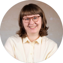 Miriam Nasri trägt eine helle Bluse, hat schulterlange Haare und eine Brille. Sie lächelt in die Kamera.